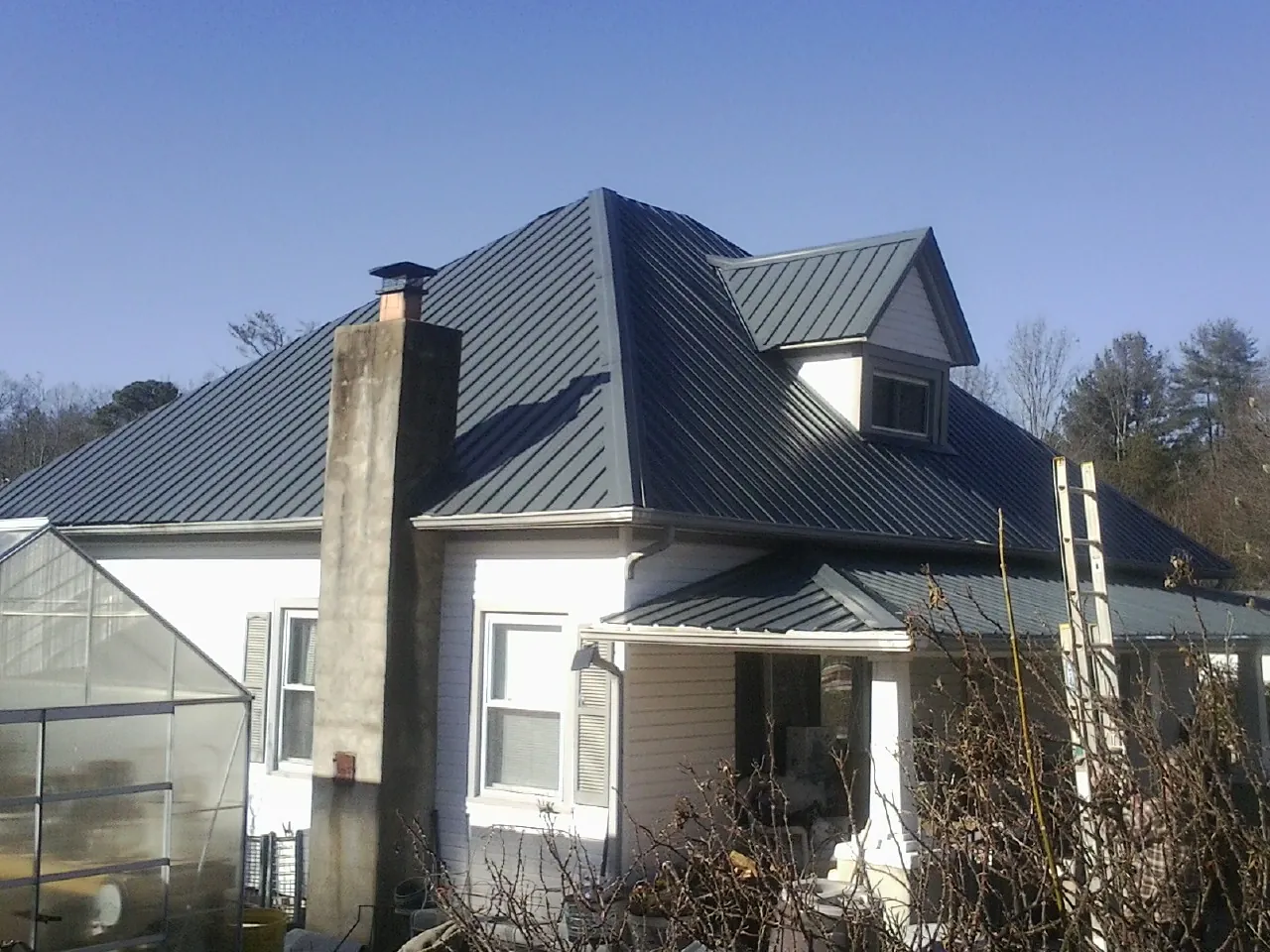 Dark blue standing seam metal roof on a white farmhouse with dormer — Slate & Tile Roof Repair by Roofing Brothers in Reinbeck