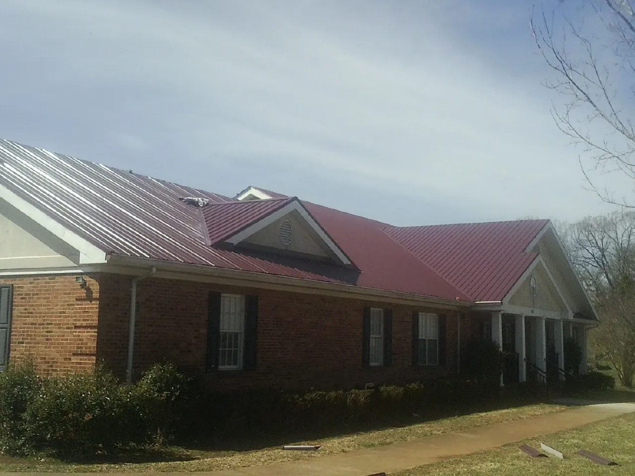 Red metal roof with gabled entries on a long brick building, from a Hail Damage Roof Repair job in Reinbeck