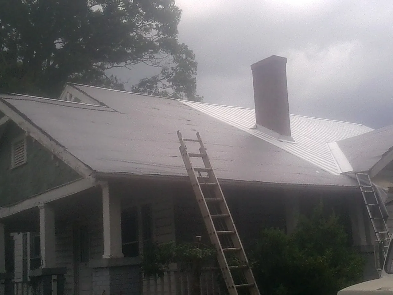 Ladders against a metal roof on an older home with a brick chimney in Reinbeck
