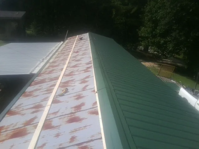 Old rusted panels beside newly installed green metal roofing — Wind Damage Roof Repair by Roofing Brothers in Reinbeck