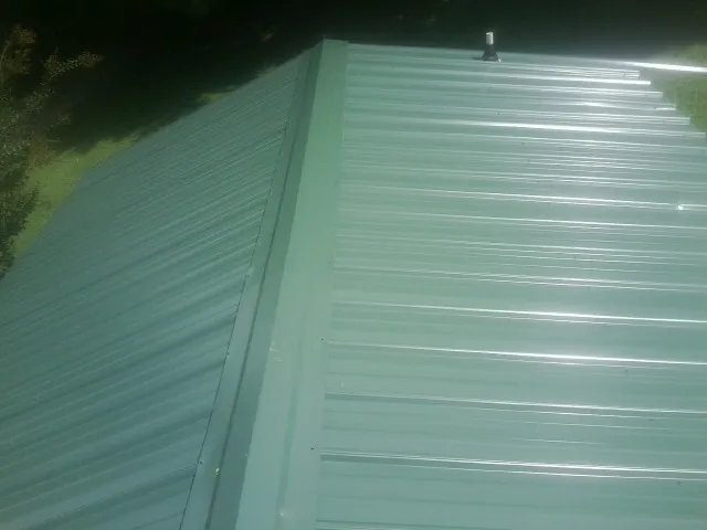 New green metal panels meeting at the ridge of a roof — Flat Roof Repair work by our crew in Reinbeck