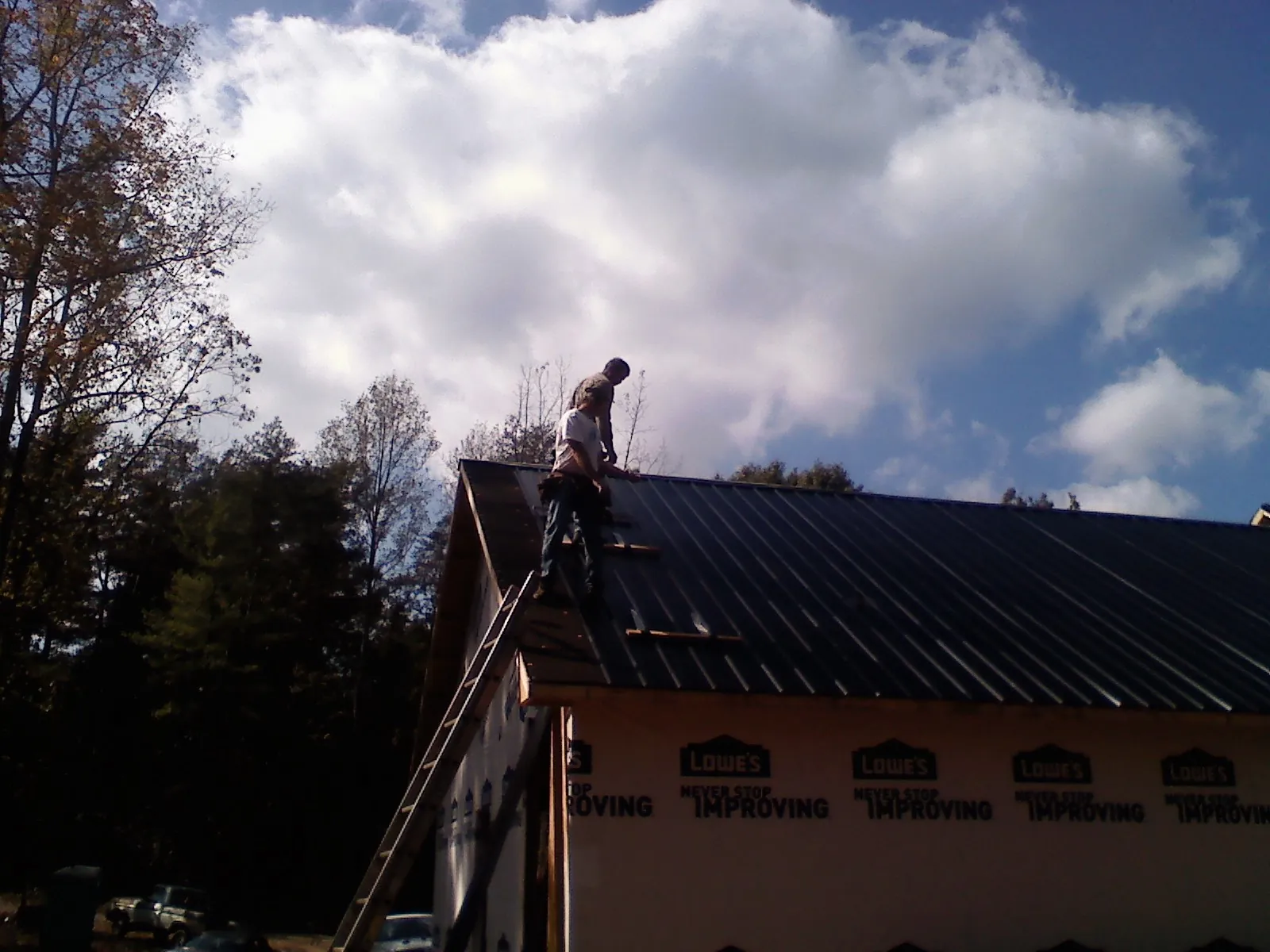 Roofer fastening dark metal panels high against a cloudy sky, from a Roof Inspection job in Reinbeck