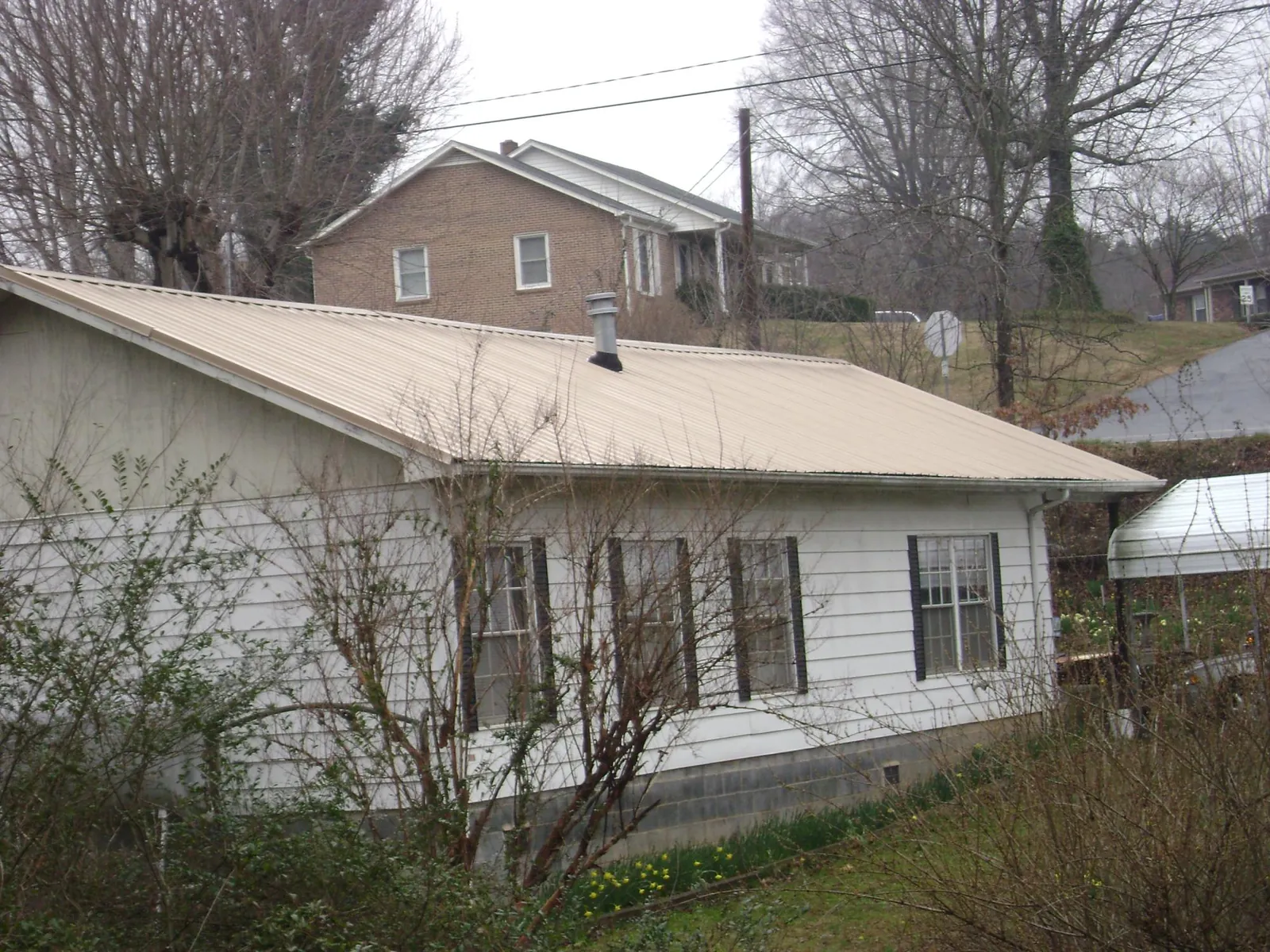 Tan metal roof on a white sided house set into a hillside — Commercial Roofing by Roofing Brothers in Reinbeck