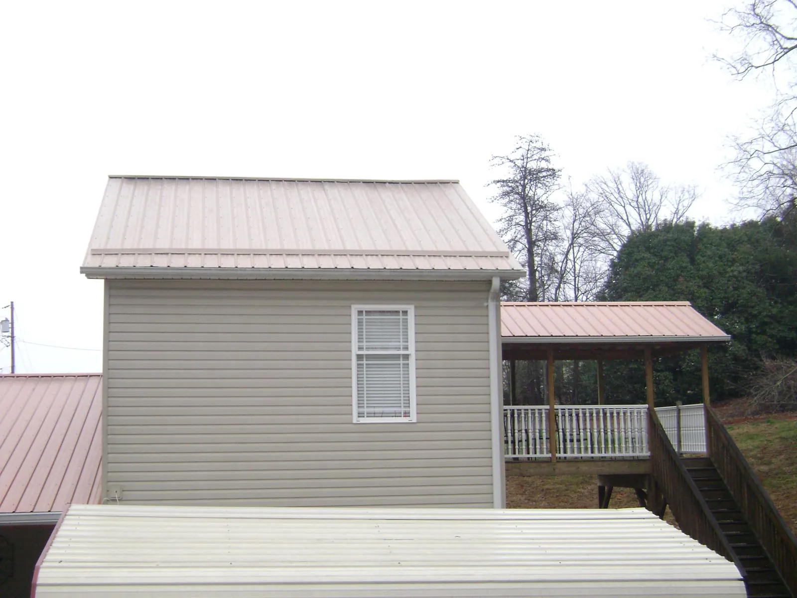 Tan metal roofs on a two story addition and attached porch, from a Roof Replacement job in Reinbeck